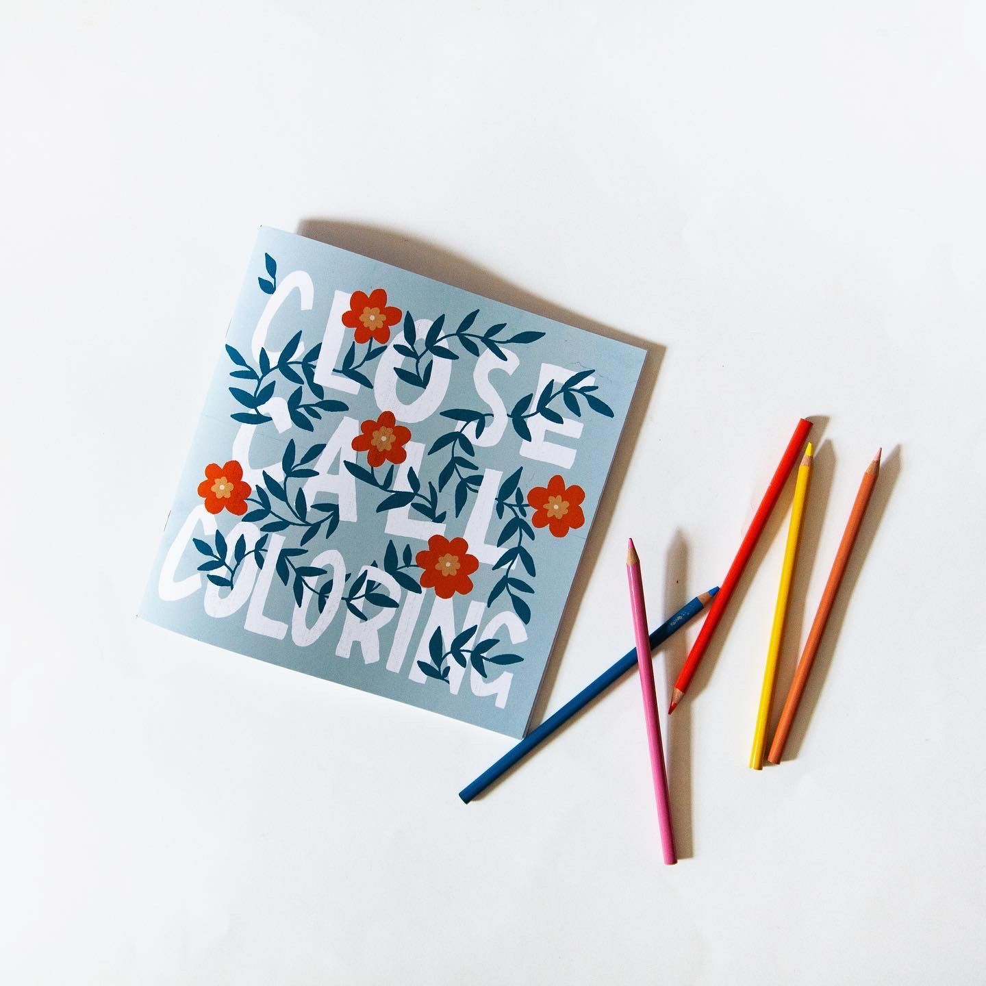 An Illustration by Amanda Adams. A coloring book with colored pencils on a table.